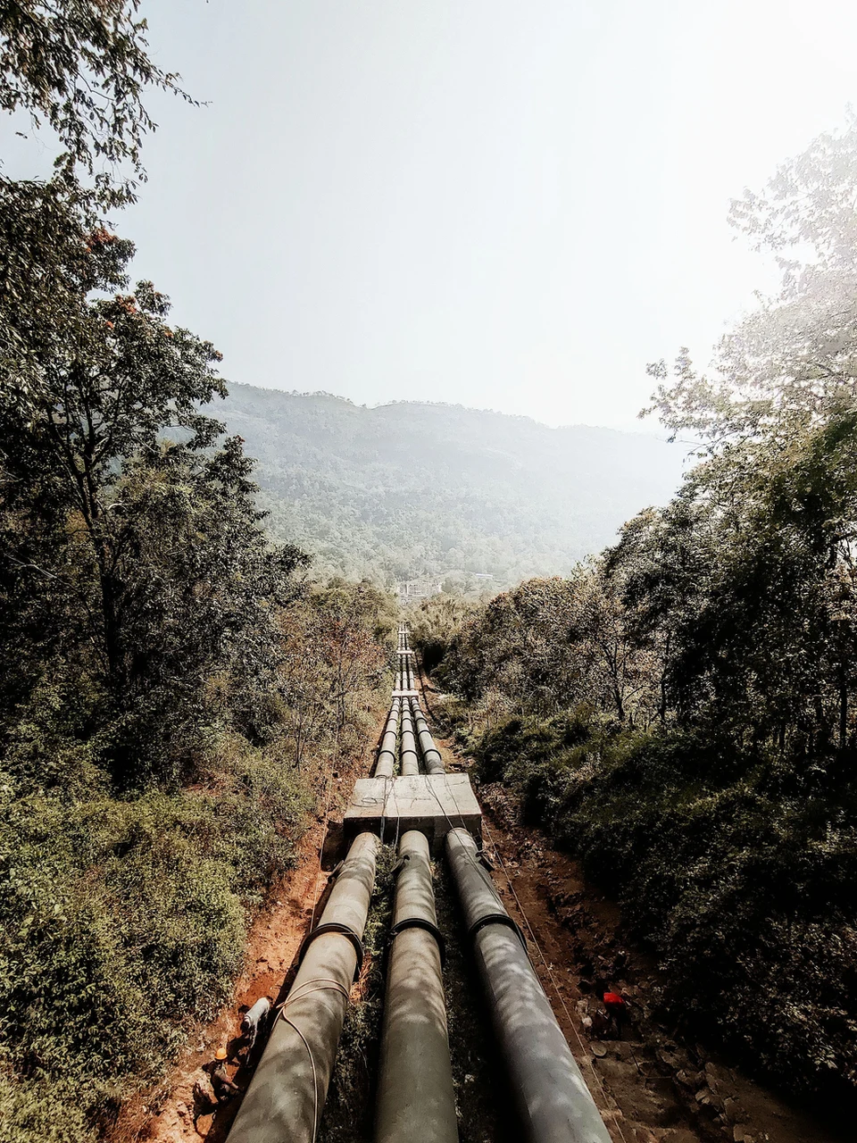 Steel cement-lined water transmission main running through forested terrain to a hillside reservoir